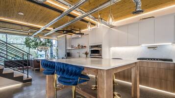 A modern kitchen with a large island, stainless steel appliances, and a bar area with blue bar stools.
