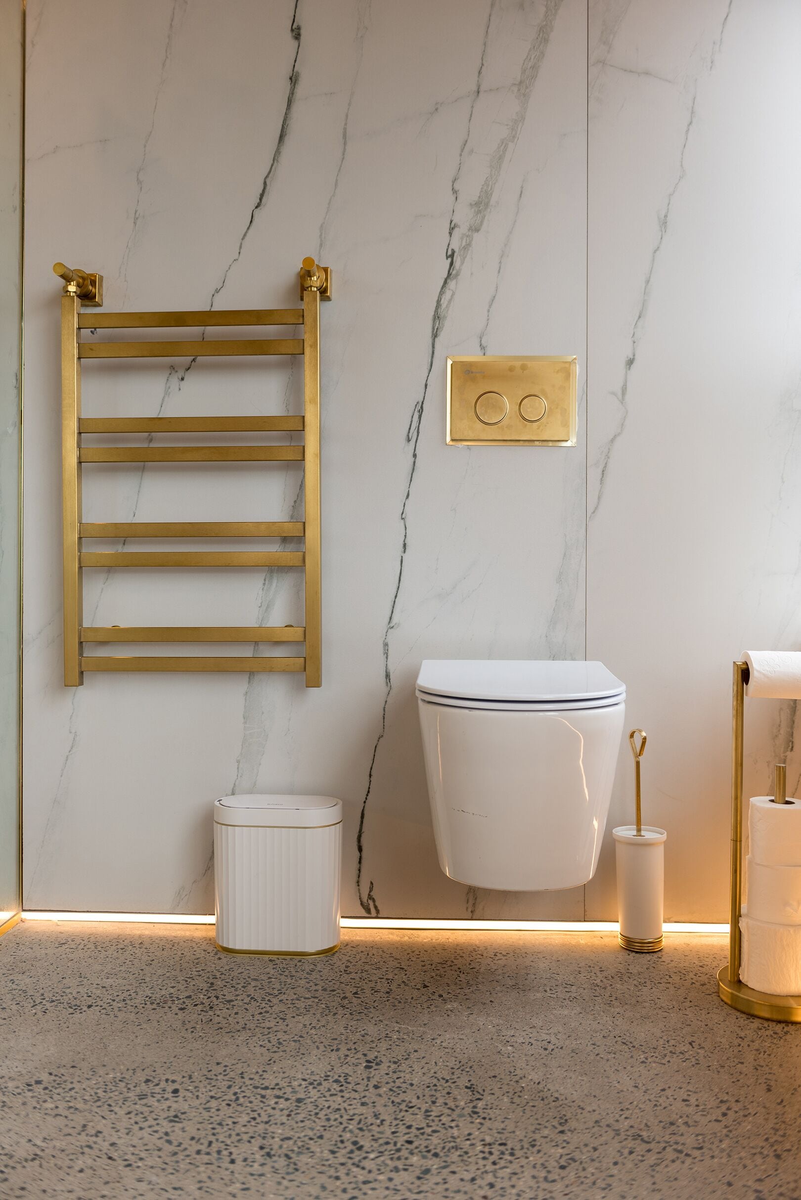 Une salle de bain avec un mur en marbre, un porte-serviettes doré, des toilettes blanches et un porte-rouleau de papier toilette doré.