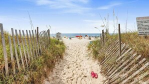 A sandy beach path with wooden fences on either side, leading to the ocean.