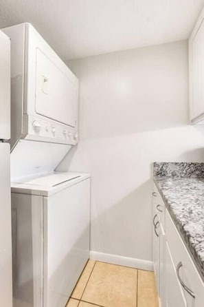 A compact kitchen with a built-in washer and dryer, a granite countertop, and white cabinetry.