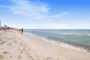 A beach with clear skies, people walking along the shore, and umbrellas set up.