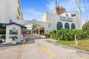 A building labeled "Sugar Beach Condominiums" with a clear entrance, a stop sign, and a directional arrow on the pavement.