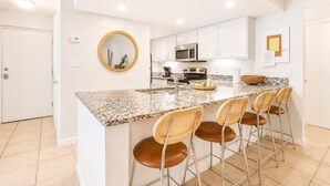 A kitchen with a granite countertop, stainless steel appliances, white cabinets, and a round mirror.