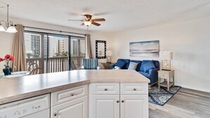 Een moderne keuken met een groot kookeiland, een zithoek met een blauwe bank, en een balkon met uitzicht op gebouwen.