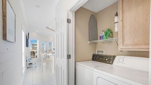 A laundry area with a washing machine, a dryer, and a shelf with cleaning supplies. - Camp David Side B- pool, beach view (Gulf Shores)