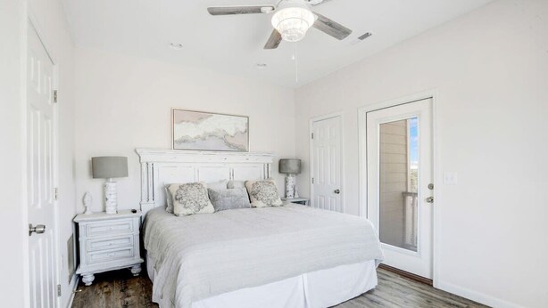 A bedroom with a bed, nightstands, a ceiling fan, and a door with a mirror. - Camp David Side B- pool, beach view (Gulf Shores)