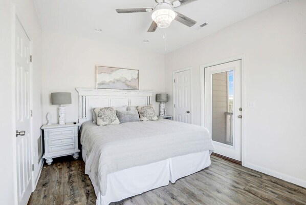 A bedroom with a bed, nightstands, a ceiling fan, and a door with a mirror.