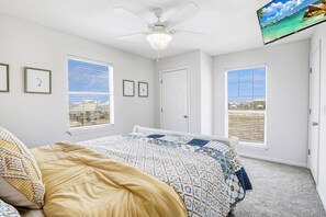 A bedroom with a bed, a ceiling fan, and two windows with blinds.