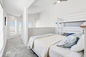 Une chambre avec un lit superposé, un ventilateur de plafond et une fenêtre avec des stores.