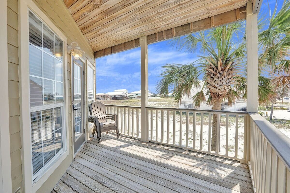 A wooden deck with a chair, overlooking a beach with palm trees.