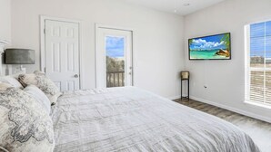 A bedroom with a large bed, a ceiling fan, a TV mounted on the wall, and a door leading to an outdoor balcony.