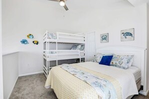 Ein Kinderzimmer mit Etagenbetten, einem Bett mit gemusterten Betttextilien und Wandbildern.