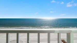 Uitzicht op het strand vanaf een balkon met een hekwerk, zee en heldere lucht.