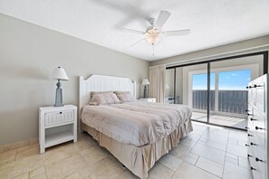 A bedroom with a bed, nightstands, a ceiling fan, and a balcony with a view.