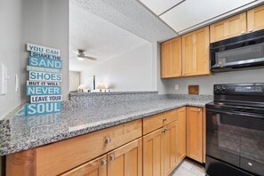 Eine moderne Küche mit Granit-Arbeitsplatten, Holzschränken, einem schwarzen Backofen und einem Deckenventilator.