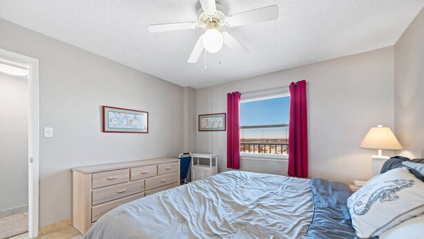 Een slaapkamer met een bed, een plafondventilator, een raam met gordijnen en een dressoir.
