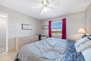 A bedroom with a bed, a dresser, a ceiling fan, a window with curtains, and a lamp.