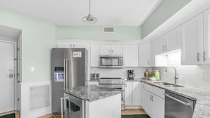 A modern kitchen with white cabinets, stainless steel appliances, a granite countertop, and a green rug.
