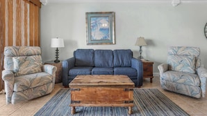 A living room with a sofa, two armchairs, a coffee table, and a painting on the wall.