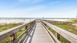 A wooden boardwalk leading to a sandy beach with a clear sky.