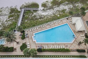 A large rectangular pool with a surrounding deck, palm trees, and a staircase leading to a building. - Pelican Pointe1204: 3BR/ 2BA, gulf-front. (Orange Beach)