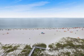A beach with a wooden boardwalk leading to the water, a sandy beach, and umbrellas. - Pelican Pointe1204: 3BR/ 2BA, gulf-front. (Orange Beach)