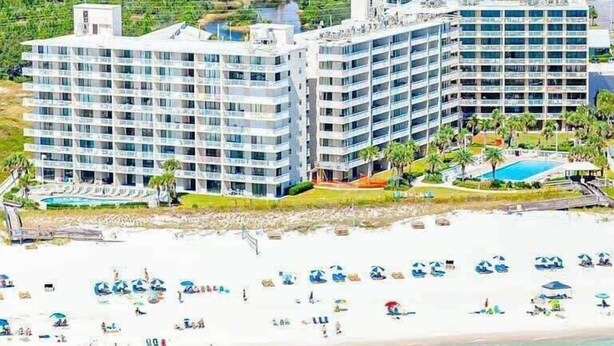 A beachfront hotel with multiple high-rise buildings, a pool, and a sandy beach with umbrellas.