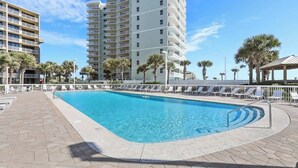 A swimming pool with lounge chairs, palm trees, and a tall building in the background.