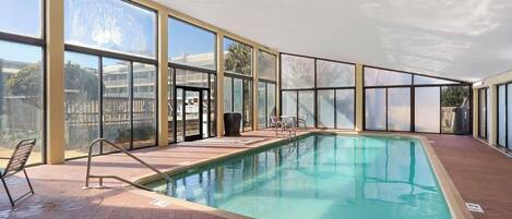 An indoor swimming pool with clear glass walls, a tiled floor, and a pool ladder.