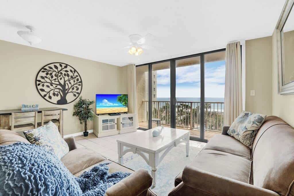 A living room with a TV, a sofa, a coffee table, and a balcony with a view.