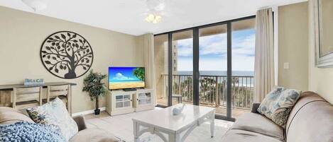 A living room with a TV, a sofa, a coffee table, and a balcony with a view.