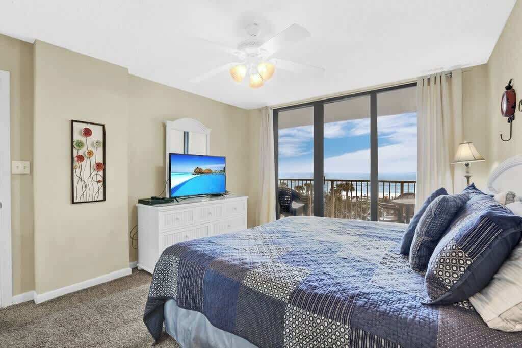 A hotel room with a large bed, a television, a ceiling fan, a balcony with a view, and a decorative wall piece.