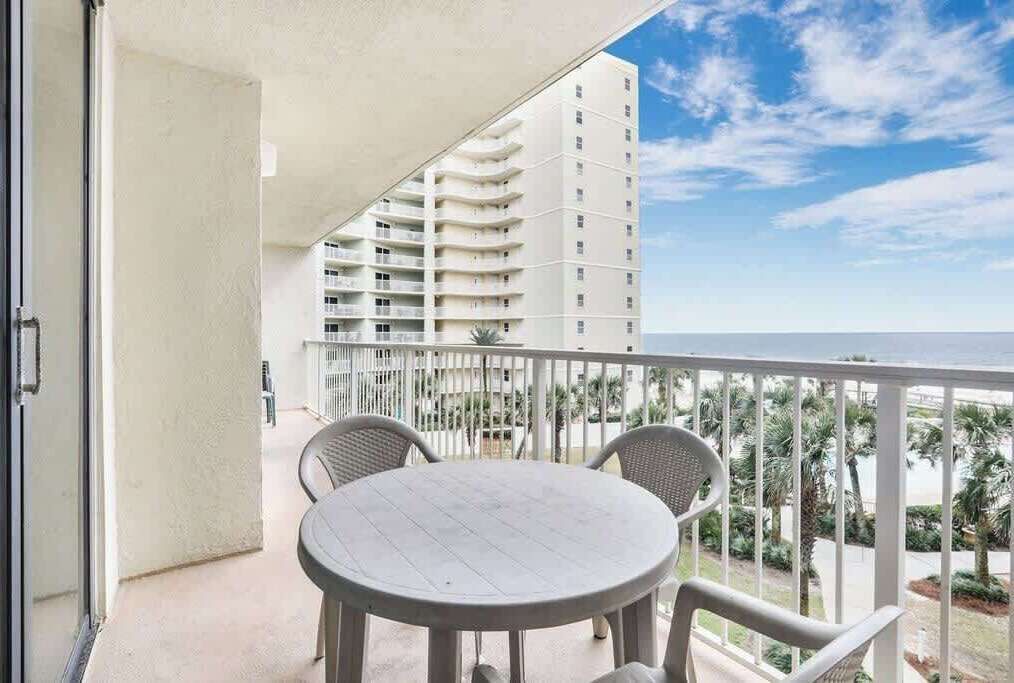 A balcony with a round table and chairs, overlooking a beach and a tall building.