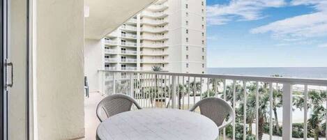 A balcony with a round table and chairs, overlooking a beach and a tall building.