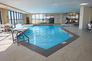 An indoor swimming pool with clear glass walls, a lifeguard station, and a seating area with chairs and a table.