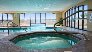 An indoor swimming pool with a hot tub, large windows, and a view of the outside. - Harbour Place 102-  gulf-view, out & indoor pool, hot tub (Orange Beach)