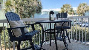 A balcony with two Adirondack chairs, a small round table, and a candle holder. - Harbour Place 102-  gulf-view, out & indoor pool, hot tub (Orange Beach)