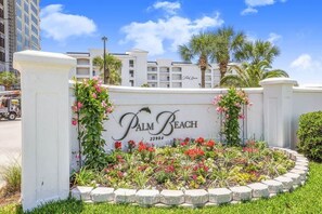 Experience the tranquil entrance of Palm Beach Hotel, surrounded by a beautifully landscaped garden with a clear view of the surrounding buildings.