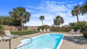 A rectangular swimming pool with a metal ladder, surrounded by white lounge chairs and palm trees.