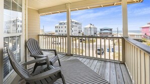 A wooden deck with two Adirondack chairs, a view of buildings across the street, and a clear sky.