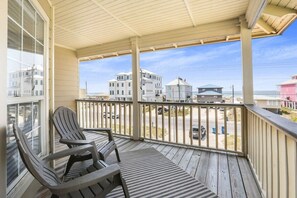 A wooden deck with two Adirondack chairs, a view of buildings across the street, and a clear sky. - Camp David Side A: pvt. pool, beach view, sleeps 9 (Gulf Shores)