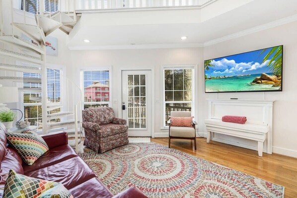 A spacious living room with a large TV, a red leather couch, patterned armchairs, and a colorful rug.