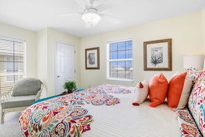 A bedroom with a bed, a chair, a ceiling fan, and two windows with blinds.