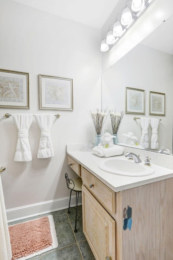 A bathroom with a vanity, sink, mirror, towel rack, and framed artwork on the wall.