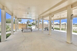 An outdoor covered patio area with concrete flooring and wooden picnic tables.