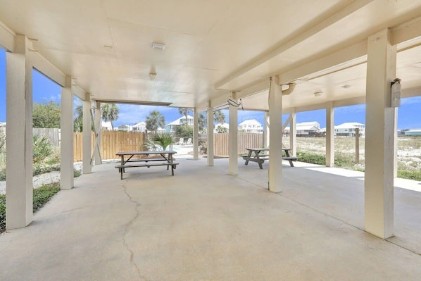 An outdoor covered patio area with concrete flooring and wooden picnic tables.