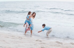 Une scène de plage où l’on voit une femme portant un enfant et une autre personne dans l’eau.