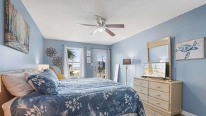 Une chambre à coucher comprenant un lit, une commode, un ventilateur de plafond et des œuvres d’art accrochées aux murs.