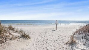 A sandy beach with a signpost, ocean waves, and clear skies.
