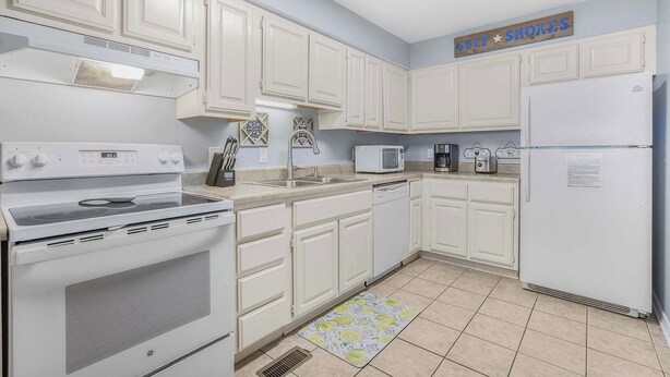 A kitchen with white cabinets, a stove, a microwave, and a refrigerator.